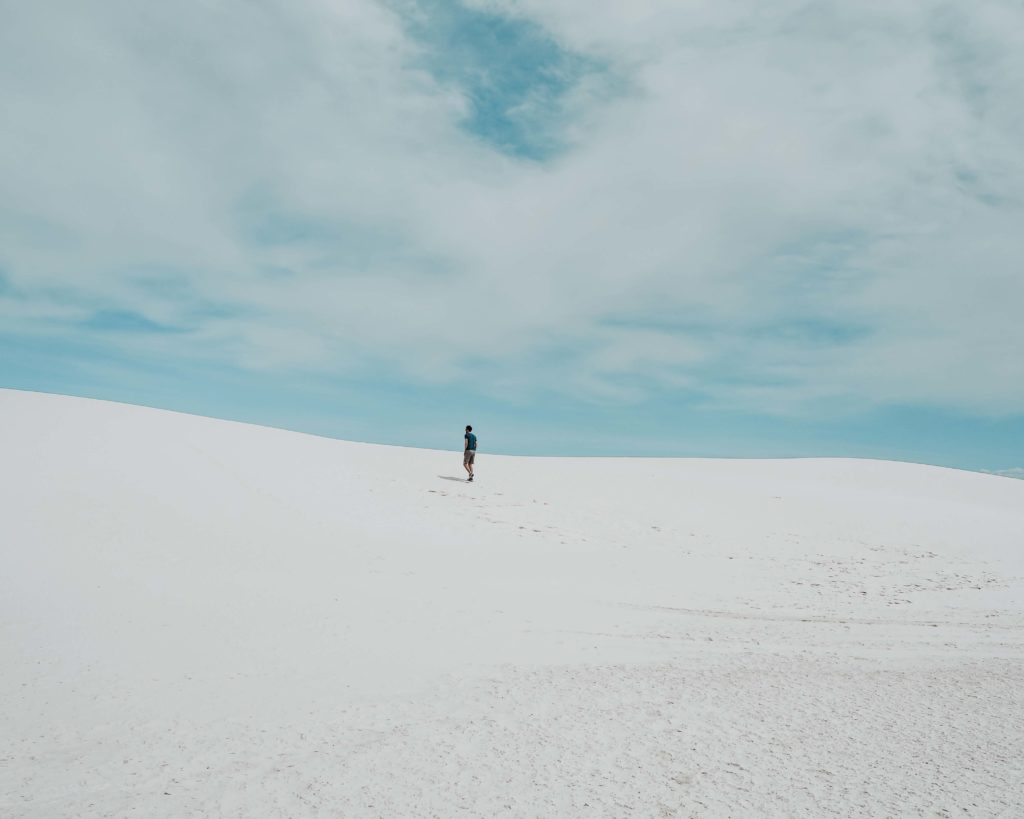 White Sands National Monument. Pictured are Sand dunes and a man walking in the distance, leaving footsteps in the sand